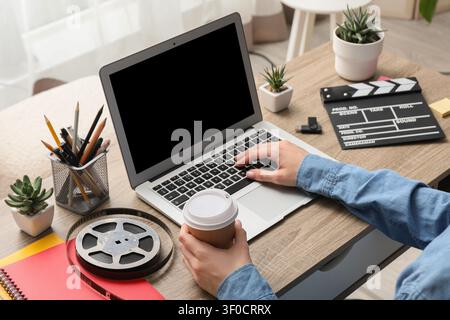 Person working on laptop with coffee and film equipment on desk Stock Photo