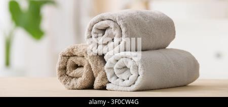 Three rolled soft towels stacked on wooden surface Stock Photo