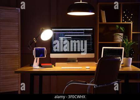 Modern workspace with computer screens displaying code at night Stock Photo