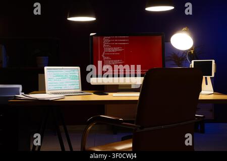 Modern workspace with computer screens displaying code at night Stock Photo