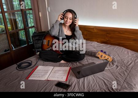 Young Musician Learning Bass Guitar with Online Lesson from Laptop at Home Stock Photo