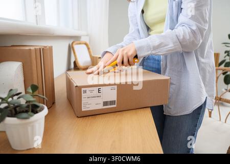 Person opening cardboard box with utility knife on wooden table Stock Photo