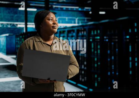 Admin working with notebook computer to do maintenance on server facility electronics processing large datasets. Stock Photo