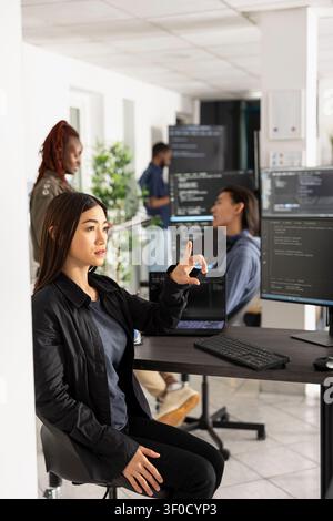 Woman developer interacts with holographic screen in futuristic office. Female programmer testing web development code on virtual interface, representing innovation and advanced digital technology. Stock Photo