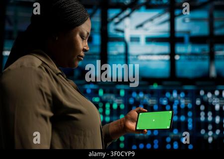 Data center programmer works with a chroma key smartphone, using an editable screen to monitor anomaly detection. Stock Photo