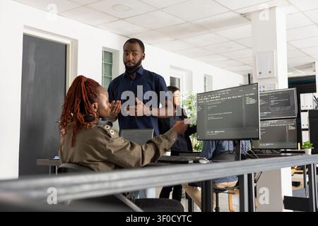African American developers work together in startup office, comparing website code on desktop pc. Focused programmers discuss strategy, technology and collaborative digital problem solving. Stock Photo