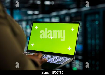 Data center programmer works with a chroma key laptop, using an editable screen to track performance metrics. Stock Photo