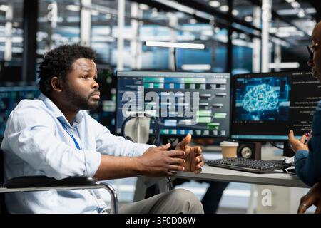 Data center manager and wheelchair user use a computer to manage machine learning workloads, working with AI technology and high performance systems. Stock Photo