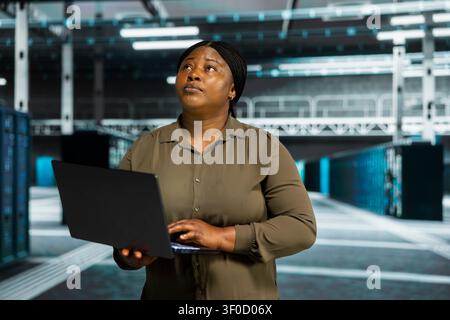 Admin working with notebook computer to do maintenance in server facility with setup helping companies stay connected. Stock Photo