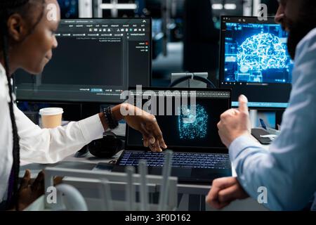 Lead software programmer and female technical specialist in computing facility updating AI automation scripts, while and african american woman programming AI algorithms at desk. Stock Photo