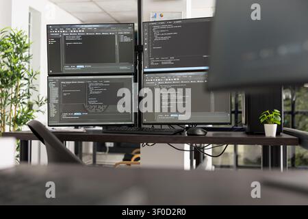 Empty IT office with several monitors displaying programming code and application data. Technology focused workspace illustrates software development, networking, and modern corporate innovation. Stock Photo