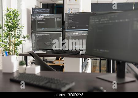 Empty office shows multiple computer screens filled with programming syntax and algorithms. Professional workspace represents web development, cybersecurity and digital business solutions. Stock Photo