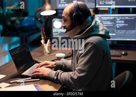 Recovering programmer listens to music and monitors online network activity on laptop, helping protect systems from security risks. Caucasian man with cervical collar checking and fixing code errors. Stock Photo