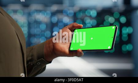 Data center administrator works with a chroma key smartphone, using an editable screen to watch a technical tutorial. Stock Photo