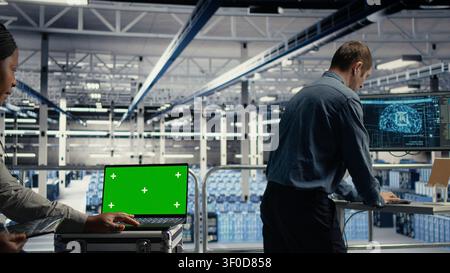 Data center technician works with a chroma key laptop, using an editable screen to monitor deep learning processes. Stock Photo