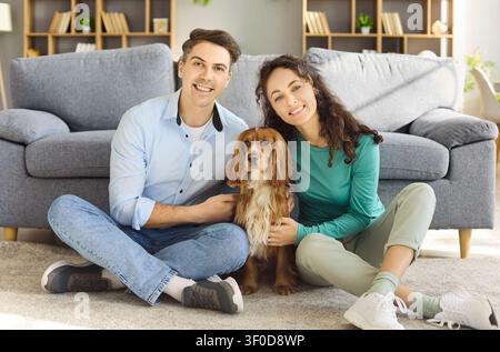 Happy young couple with cocker spaniel relaxing on living room floor at home Stock Photo