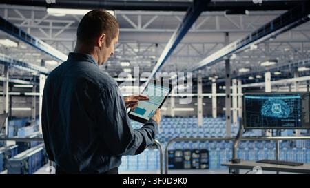 IT expert uses a tablet touchscreen in a server room to review data charts and monitor equipment health. Stock Photo