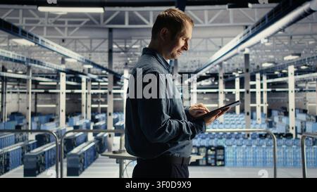Data center technician uses a tablet in a server room to review test results and confirm reliable system operation. Stock Photo