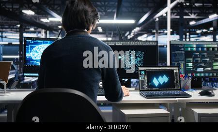 System admin entering computing facility office, checks AI diagnostics on computer, while starting work at server facility desk, enhancing AI systems configuration. Stock Photo