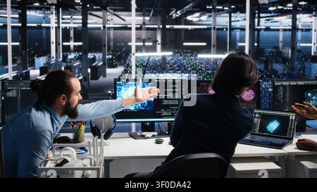 Data infrastructure center team of engineers trying to resolve urgent system alert while working with AI with collaborative team members repairing software fault popup while working with AI tech. Stock Photo