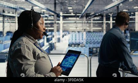 Data center technical support staff member working with AI on a digital tablet to guide customers. Technical specialist in server facility helps users fix system errors on servers applying AI. Stock Photo