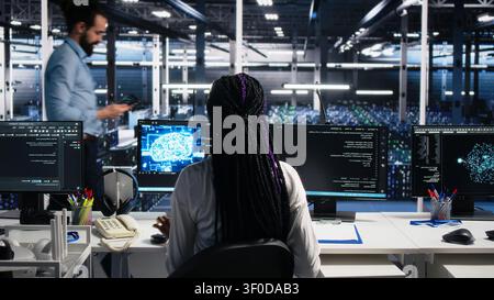 Female software programmer in computing facility checks AI diagnostics, assessing neural network operational performance, while optimizes AI systems configuration. Stock Photo