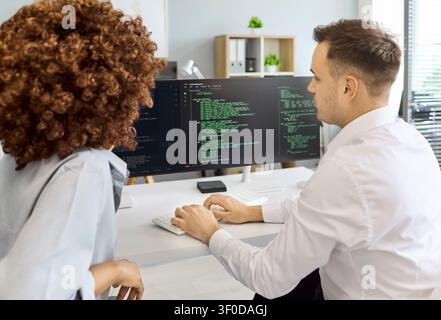 Developers Reviewing Code on Dual Monitors in Office, Team Collaboration Session Stock Photo
