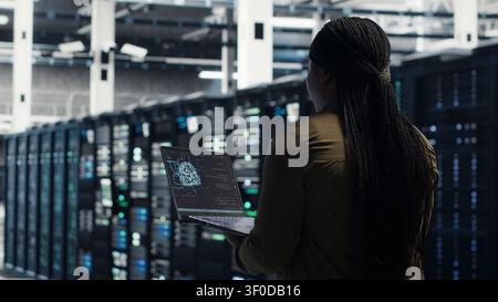 Software developer uses laptop-based deep learning tools in a server room to improve AI operations and system efficiency. Stock Photo