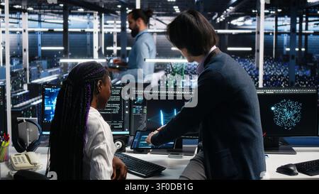 Asian man programs on a computer workstation in a data center with generative AI assistance. Stock Photo
