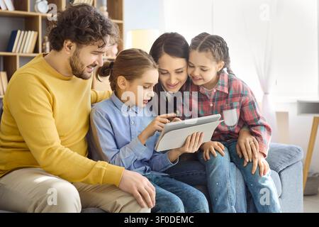 Happy parents and daughters using tablet at home for online learning and bonding Stock Photo