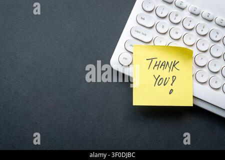 Thank you on yellow note on top of keyboard, dark color background. Copy space. Stock Photo