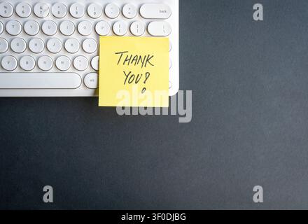Thank you on yellow note on top of keyboard, dark color background. Copy space. Stock Photo