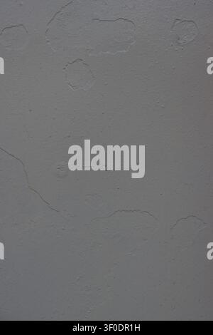 Vertical background texture of a grey concrete wall featuring rough plaster, noticeable surface cracks, and uneven peeling paint defects, perfect for Stock Photo