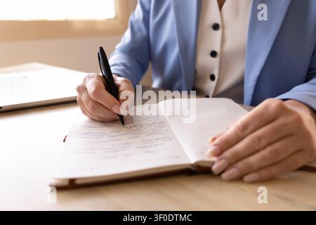 Woman writing notes in notebook at office desk, closeup Stock Photo