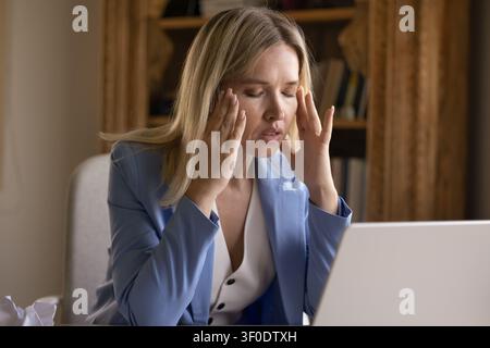 Older adult businesswoman experiences severe headache at workplace desk Stock Photo