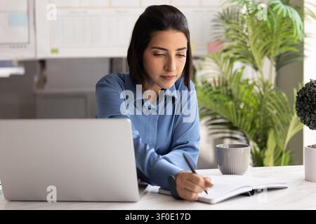 Businesswoman writing notes sitting at office desk with laptop Stock Photo
