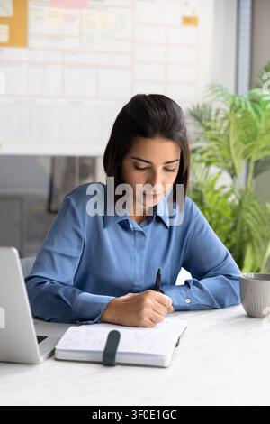 Focused business woman writing notes at desk Stock Photo