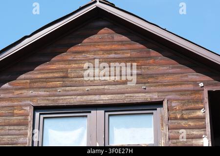 Close-up view of a rustic wooden house facade featuring weathered timber cladding, traditional window and clear blue sky on a sunny day. Stock Photo