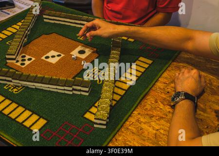 A high-angle close-up shot of players setting up a Mahjong game, featuring stacked tile walls on a green mat and a pair of dice rolled on the table ce Stock Photo