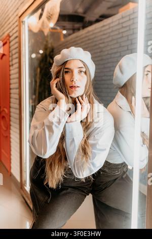 Woman beret mirror Stylish young woman posing in front of a neon lit mirror inside a modern cafe setting Stock Photo