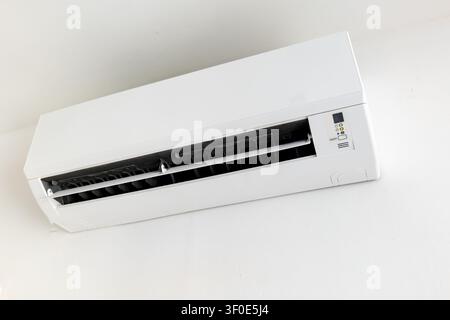 Wall-mounted split air conditioner unit on white wall, indoor climate control Stock Photo