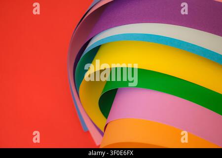 Colorful curved sheets of paper forming a smooth wave pattern on a red background. Showing bright rainbow tones, creative design and modern abstract c Stock Photo