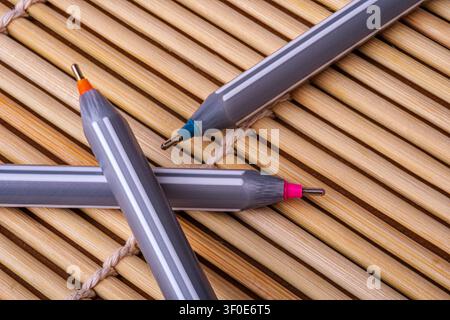 Three fine-liner pens with grey and white striped bodies and colored tips are arranged on a bamboo mat. Highlighting the contrast between the modern w Stock Photo