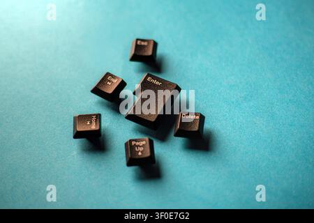 Scattered black keyboard function keys like Enter, Delete, and Home rest on a bright aqua blue background. Symbolizing hardware failure and technology Stock Photo