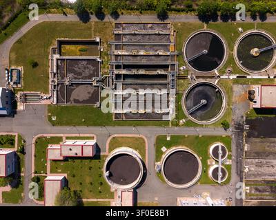 The view shows a water treatment plant featuring several circular tanks and processing units. Green spaces surround the facility, with structures alig Stock Photo