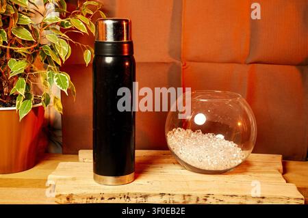 Black thermos bottle and glass bowl with ice on a wooden surface Stock Photo