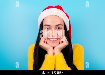 Photo of excited charming girl dressed yellow fluffy sweater red cap arms cheeks smiling isolated blue color background Stock Photo