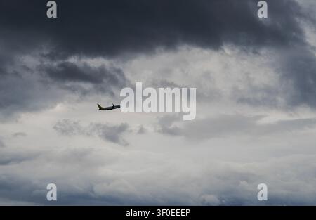 Passenger airplane flying high through a dramatic, cloudy dark sky at sunset Stock Photo