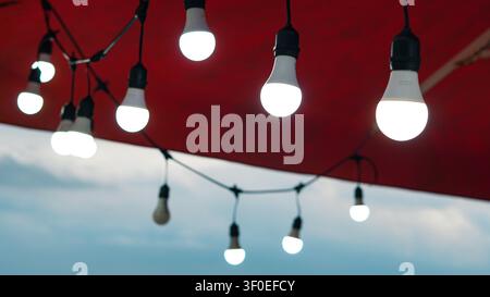 Glowing LED string lights suspended under a red canopy outdoors at twilight Stock Photo