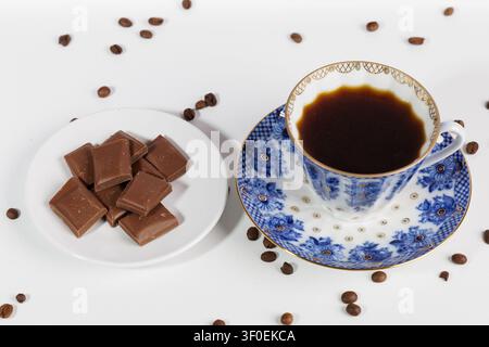 A porcelain pairing sits on a white table: a cup of strong espresso and chocolate. Stock Photo